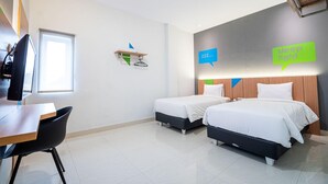 Habitación de hotel con dos camas, un escritorio y una silla. Se ve una ventana y un estante con un bolso colgado.