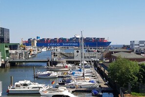 A marina with a large cargo ship docked, surrounded by smaller boats and dockside buildings. - Holiday apartment with 4 bedrooms (Cuxhaven)
