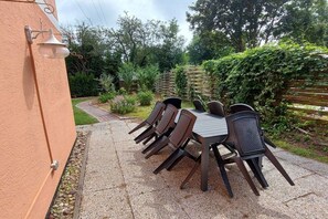 An outdoor patio with a round table and chairs, surrounded by a garden and a wooden fence. - Holiday apartment with 4 bedrooms (Cuxhaven)