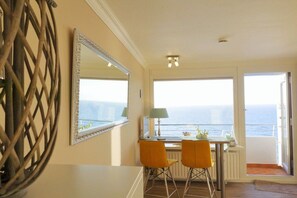 Ein Zimmer mit Essbereich, zwei Stühlen, einem Tisch, einem Spiegel und Meerblick.