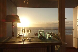 A table with a glass of wine, two glass jars, and a candle, overlooking a sunset over the sea. - Sylt Dream Sea View Metropol (Westerland)
