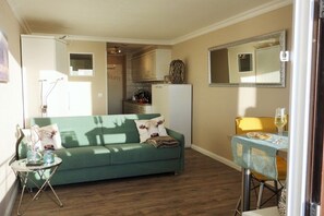A compact living space with a sofa, a dining table, and a kitchen area. - Sylt Dream Sea View Metropol (Westerland)