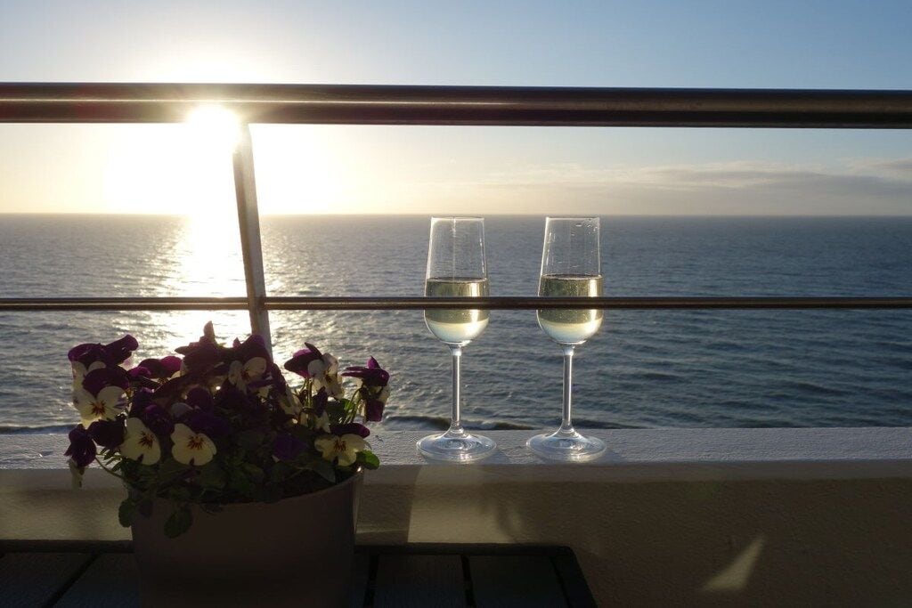 Un balcón con vista al océano y dos copas de vino blanco.