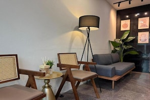 A modern lounge area with a sofa, two chairs, a floor lamp, and a small table with a plant and a box of candles. - Ibilik Hotel @ Johor Bahru (Johor Bahru)