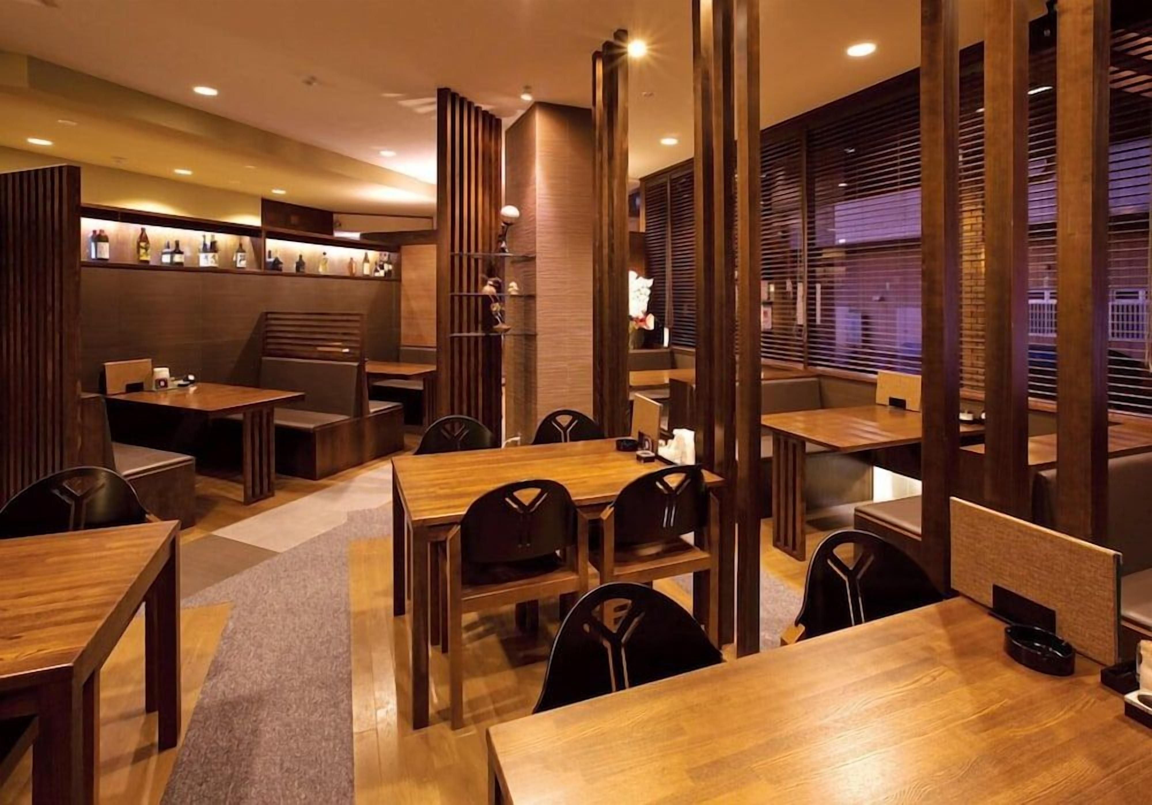 A restaurant with wooden furniture, recessed lighting, and a brick wall.