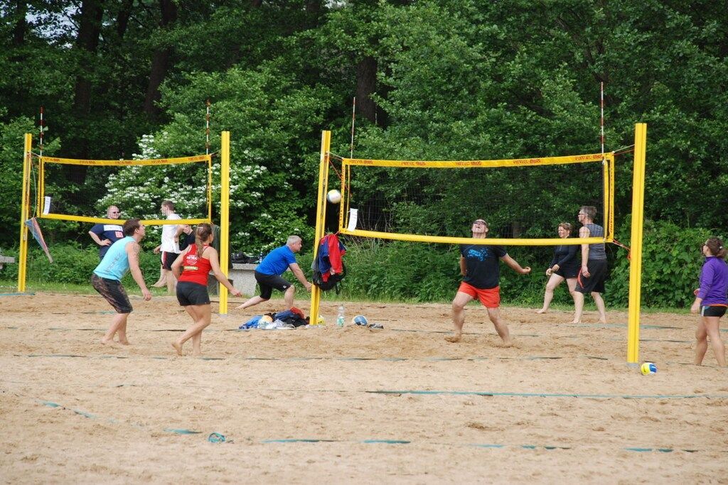 Un groupe de personnes joue au volleyball sur un terrain de sable, avec des arbres en arrière-plan.