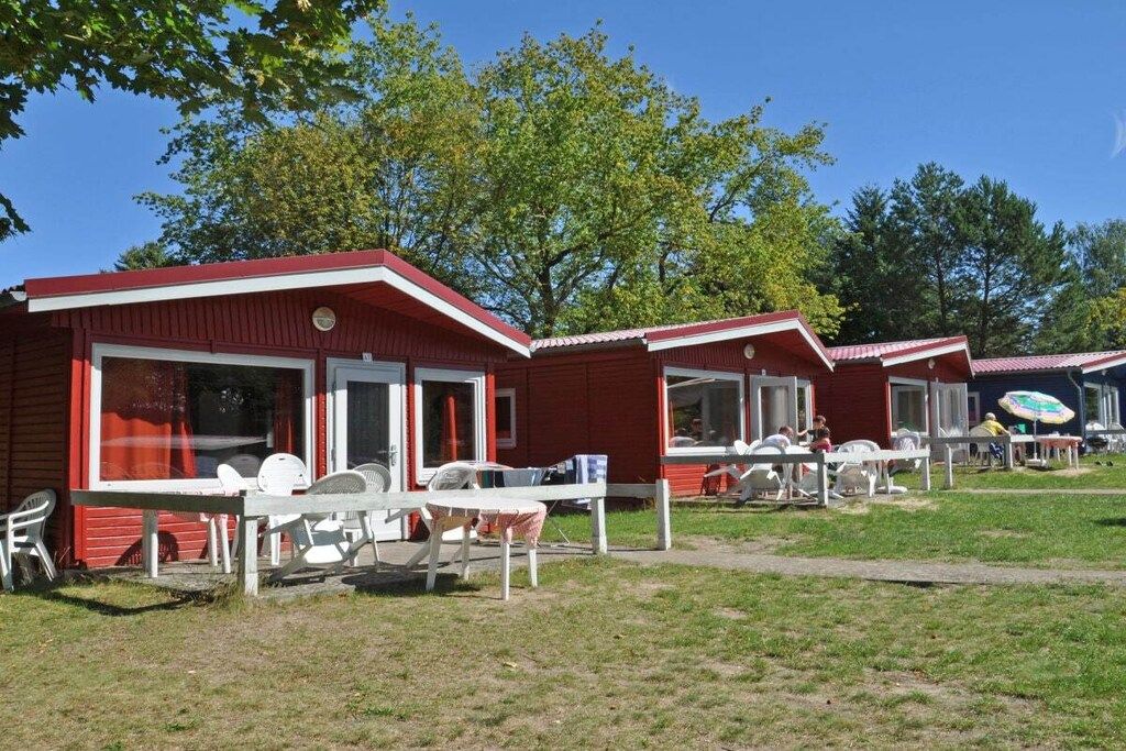 A row of red cabins with white-framed windows and doors, outdoor seating, and a clear sky.