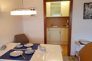 Ein Essbereich mit einem für vier Personen gedecktem Tisch, eine durchgehende Tür zur Küche und ein gerahmtes Bild an der Wand.