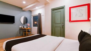 Habitación de hotel con cama, escritorio con silla, espejo, ventana con cortinas y puerta.