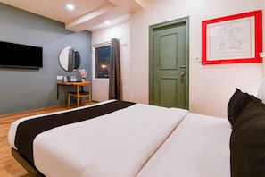 Ein Hotelzimmer mit Bett, Schreibtisch mit Stuhl, Spiegel, Fenster mit Vorhängen und einer Tür.