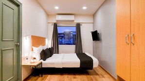 Una habitación de hotel con cama, mesita de noche, lámpara y televisión montada en la pared.