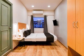 Ein Hotelzimmer mit Bett, Nachttisch, Lampe und einem an der Wand befestigten Fernseher.