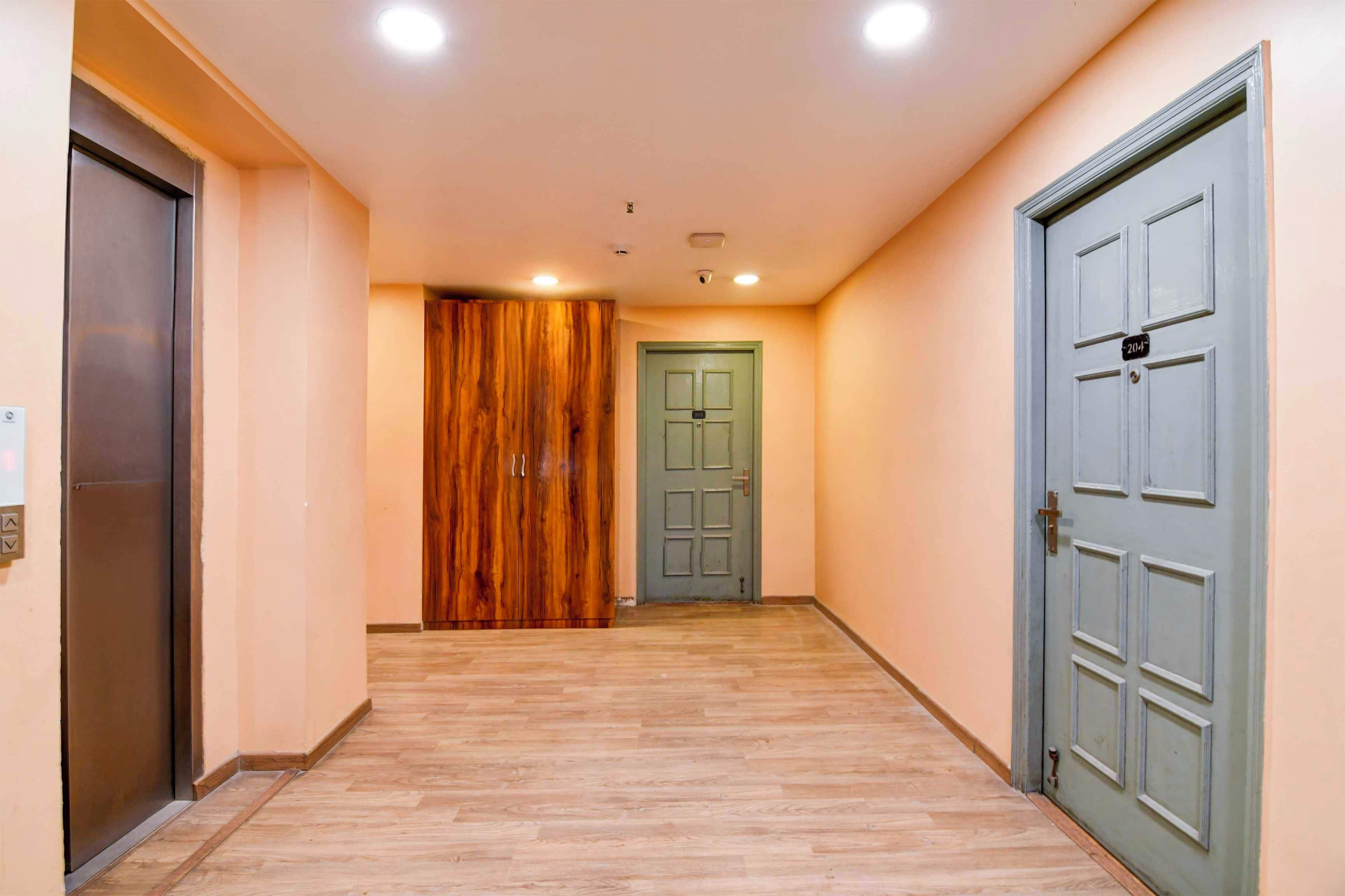 A hallway with wooden flooring, a green door, and a grey door with a number plate.