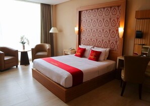 A hotel room with a large bed, two bedside tables, a desk, a chair, and a lamp.