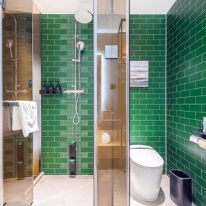 A modern bathroom with green tiled walls, a glass shower enclosure, a white toilet, and a black trash bin. - Atour X Hotel, Majiabao Metro Station, Beijing South Railway Station (Beijing)