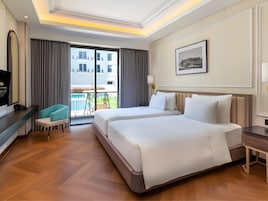 Habitación de hotel con una cama grande, un escritorio, una silla, un televisor y un balcón con vistas a edificios.