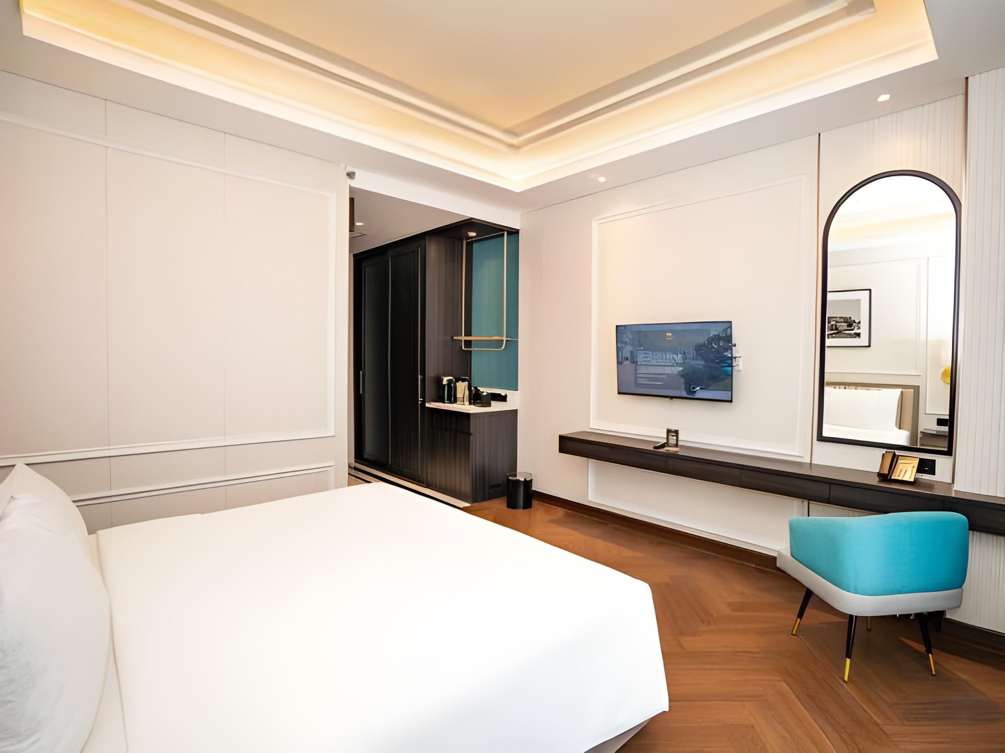 Habitación de hotel con una cama grande, un televisor, un espejo y un baño visible a través de una puerta abierta.