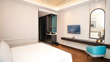 Habitación de hotel con una cama grande, un televisor, un espejo y un baño visible a través de una puerta abierta.