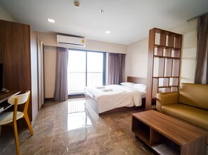 A hotel room with a bed, a desk, a chair, a sofa, an air conditioning unit, and a view of the outside. - Rangsit Residence & Hotel (Thanyaburi)