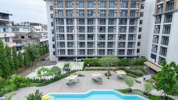 A modern building with multiple floors, a swimming pool, and surrounding greenery.
