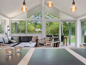 Une pièce spacieuse avec un plafond haut, de grandes fenêtres, un canapé d’angle, une table à manger et une cheminée.