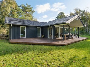 Une maison moderne dotée d’une grande terrasse, d’un espace repas extérieur couvert et d’un garage.