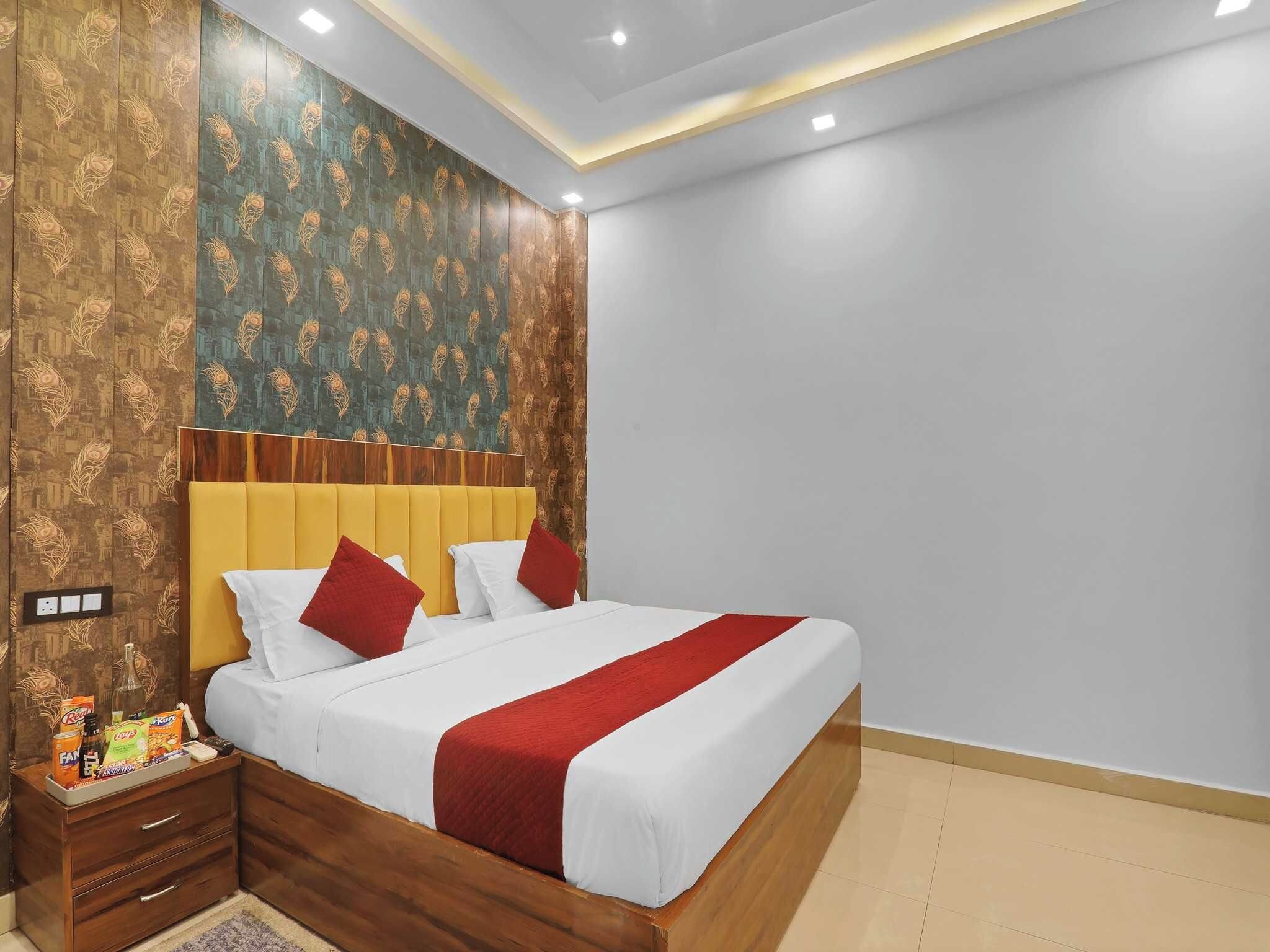 A hotel room with a bed, wooden headboard, and a nightstand with a bottle and snacks.