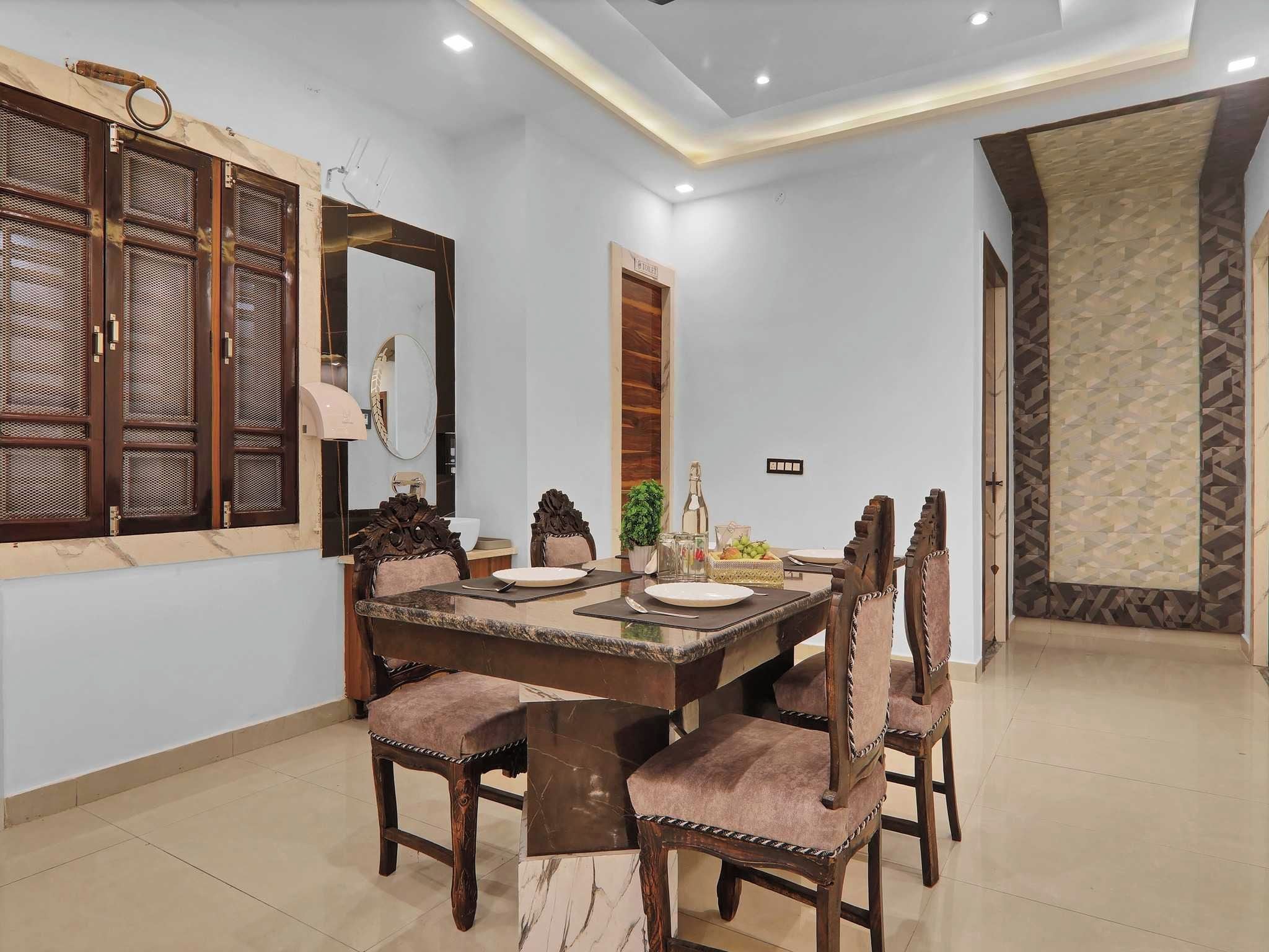Un comedor con una mesa de mármol, sillas de madera, un espejo grande y una puerta decorativa.