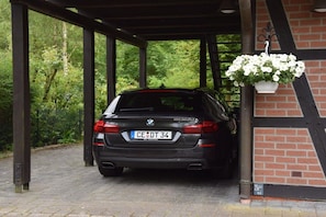 A black car parked under a covered area with a brick wall and greenery in the background. - Holiday apartment with 1 bedroom (Winsen)