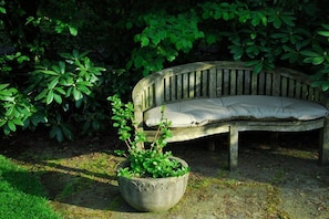 A wooden bench with a cushion, surrounded by lush greenery and a potted plant. - Holiday apartment with 1 bedroom (Winsen)