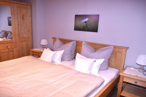A neatly made bed with a headboard, a bedside table with a lamp, a wooden wardrobe, and a framed picture on the wall. - Holiday apartment with 1 bedroom (Winsen)