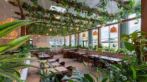 Een restaurant interieur met houten balken, hangplanten en grote ramen.