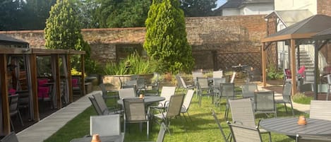 An outdoor patio with multiple tables and chairs, surrounded by a brick wall and greenery.