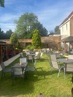 An outdoor patio with multiple tables and chairs, surrounded by a brick wall and greenery.