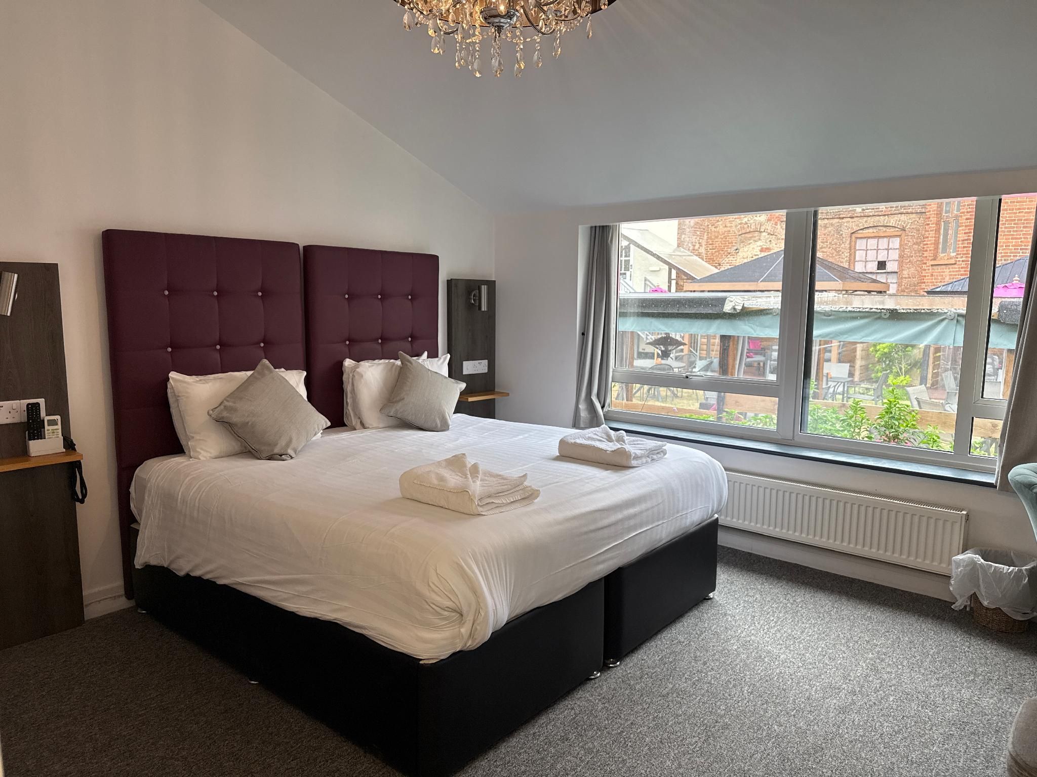 A modern bedroom with a large bed, a dark headboard, and a view of the outside.