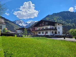 Un hotel con vistas a la montaña, que cuenta con un edificio grande con múltiples ventanas y balcones, rodeado de vegetación exuberante y un cielo despejado.