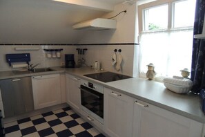 Une cuisine avec un carrelage à motifs, des appareils électroménagers en acier inoxydable, une fenêtre avec des rideaux et un meuble blanc.