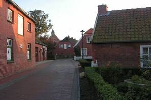 Une rue étroite bordée d’immeubles en briques rouges, une clôture blanche en bois et, au loin, le clocher d’une église.