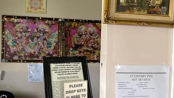 A hotel reception area with a framed artwork, a notice board with a message, and a sign for Economy Inn.
