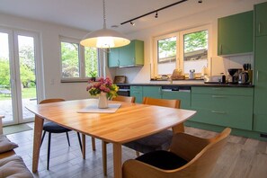 A modern kitchen with green cabinets, a wooden dining table, and a pendant light. - Garden (Holiday home Haldern) (Rees)
