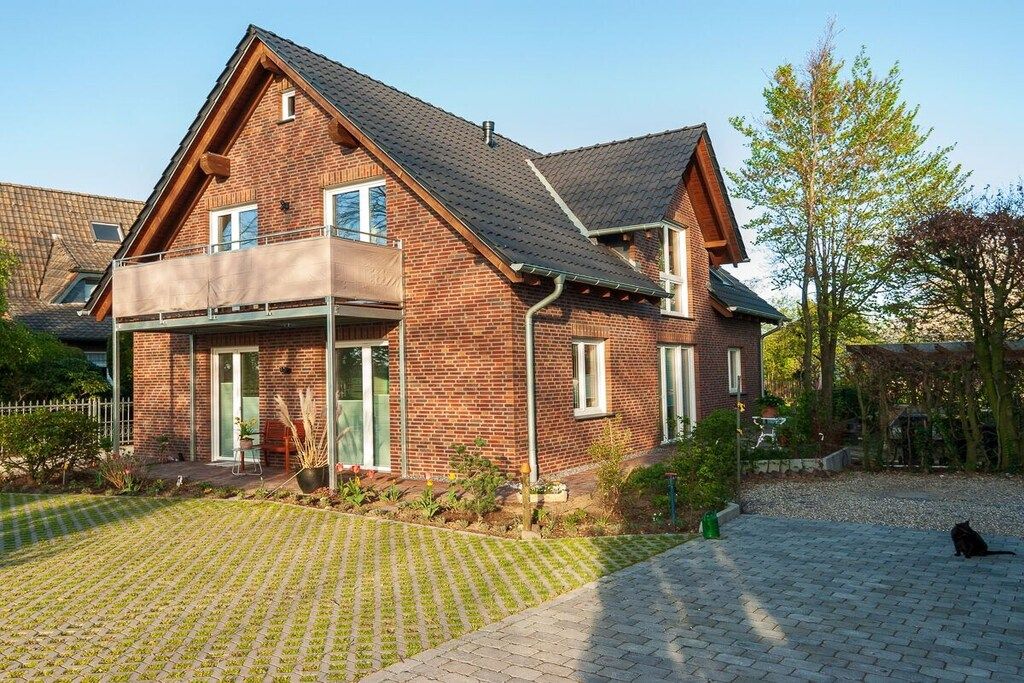 A two-story brick house with a balcony, a paved driveway, and a cat in the foreground.