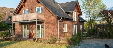 A two-story brick house with a balcony, a paved driveway, and a cat in the foreground.