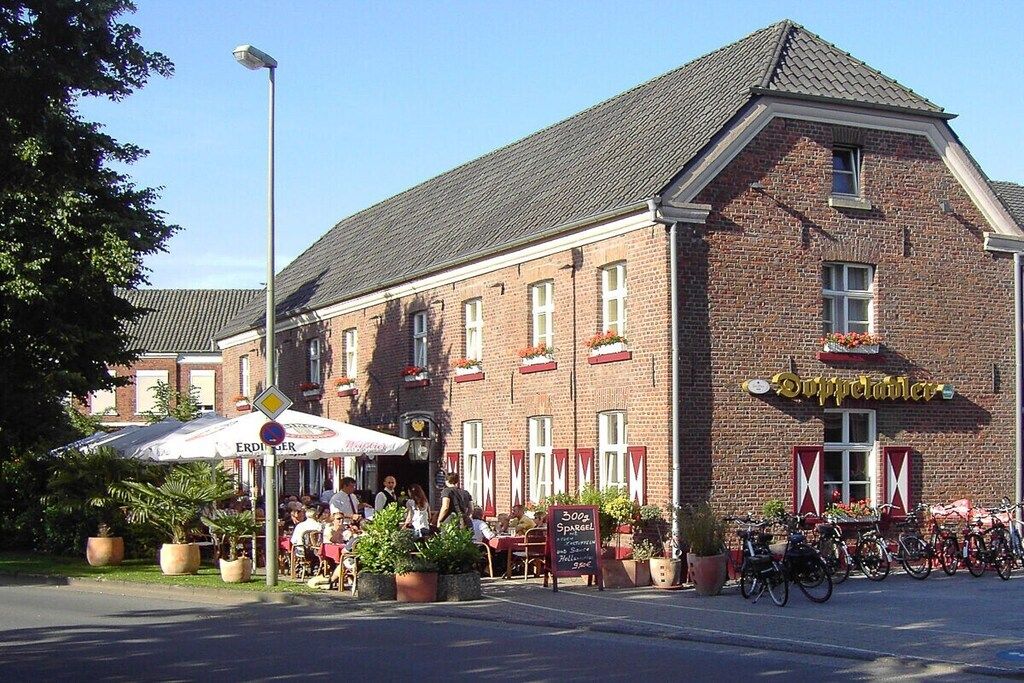 A brick building with a sign that reads 'Supperlander.' There are outdoor tables and chairs, potted plants, and bicycles parked outside.