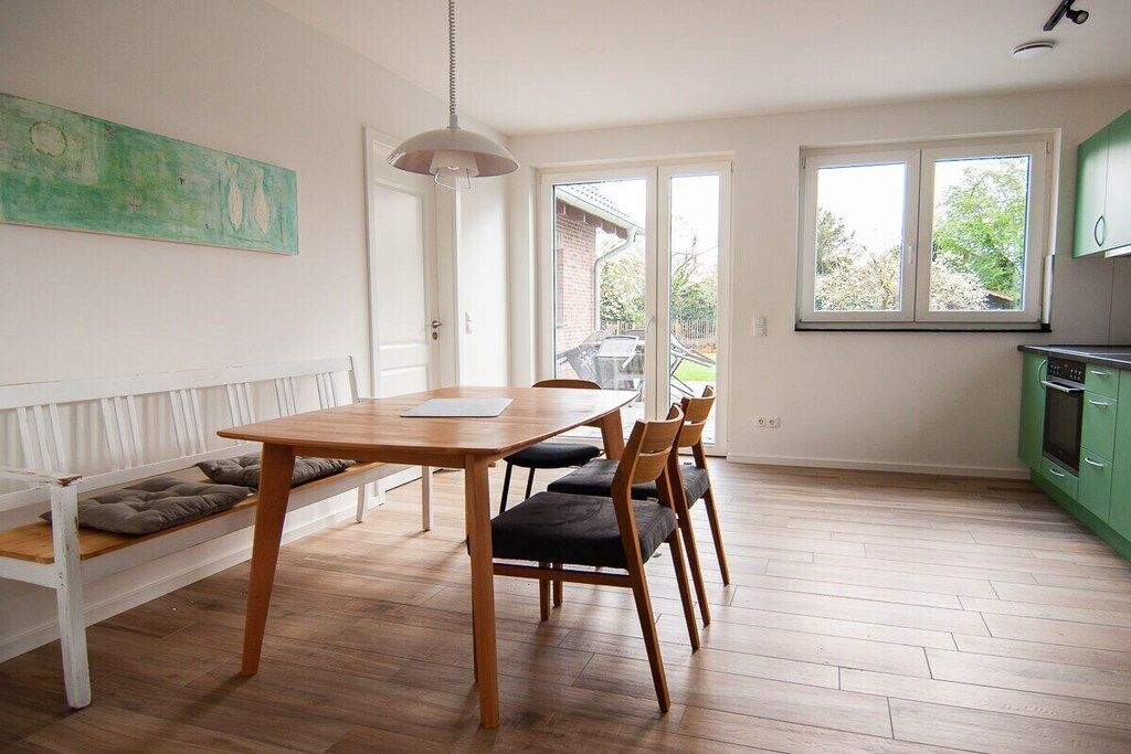 A dining area with a wooden table and chairs, a bench with cushions, a pendant light, and a view through a glass door to the outside.