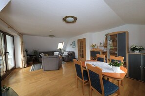 A living room with a sofa, a dining table with chairs, a cabinet, and a window with curtains. - Holiday apartment with 1 bedroom (Cuxhaven)