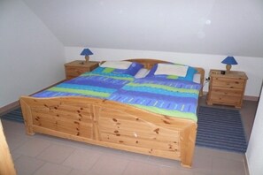 A wooden bed with a colorful quilt, two bedside tables with lamps, and a blue mat on the floor. - Holiday home family Leitner (Burhave)