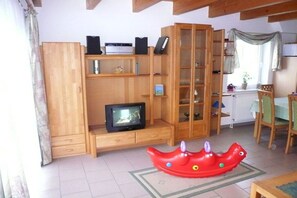 A living room with wooden furniture, a television, and a red children's toy. - Holiday home family Leitner (Burhave)