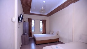 Habitación de hotel con cama, televisor, armario y ventana con cortinas.