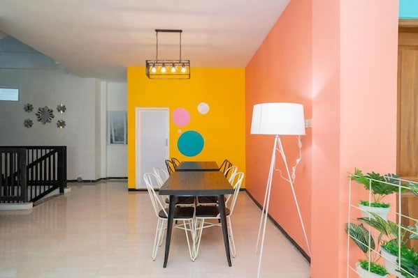 A dining area with a table and chairs, a floor lamp, and a wall with circular decorations. - Sans Hotel Queen Batu (Batu)