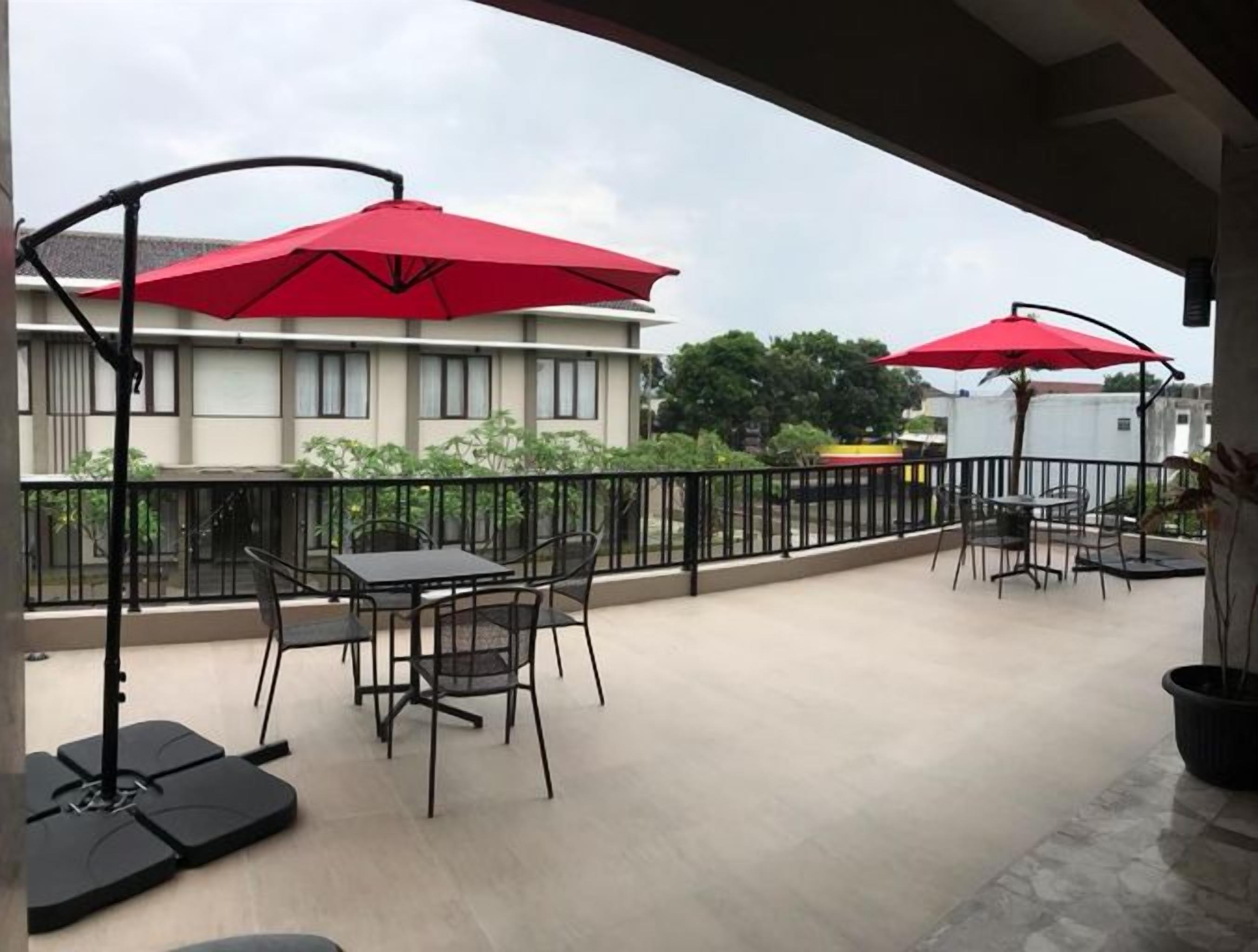 Un espace extérieur aménagé en terrasse, avec des tables et des chaises, des parasols rouges et une vue sur les bâtiments.